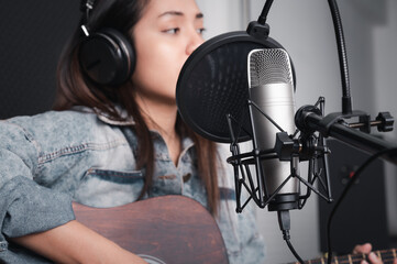 Asian female singer with a passion for music and microphone. While playing her guitar in a professional studio. Music concept, sound recording concept.