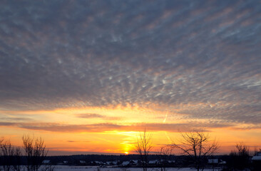 Fototapeta premium Golden rays of the sun in the sky with cumulus clouds over the village on a winter evening, rural landscape