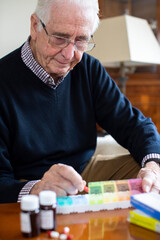 Senior Man At Home Organizing Medication Into Pill Dispenser