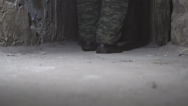 The feet of a man walking down the dark corridor of an old abandoned basement. Rear view. Low key