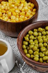 Bowls of boiled sweet corn and green peas and their sauce on a white tablecloth