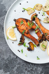 Grilled salmon steak with lemon, spices and lime in a white plate on a stone slate table. Deliciously cooked salmon fillet.