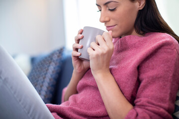 Young Woman Relaxing On Sofa At Home With Hot Drink