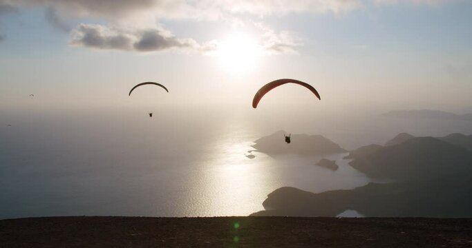 Paragliders fly from the mountain to a great height during sunset, in front of seascape and mountains. Slow motion