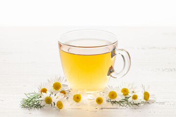 Chamomile tea and flowers in a glass cup on a white background.