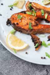 Grilled salmon steak with lemon, spices and lime in a white plate on a stone slate table. Deliciously cooked salmon fillet.