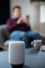 Man Streaming Music Or Podcast To Smart Speaker From Mobile Phone At Home
