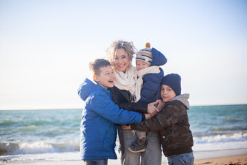 Fototapeta na wymiar Happy family, mother with sons walking wirh fun in the sea shore on windy day. People dressed warm clothes.