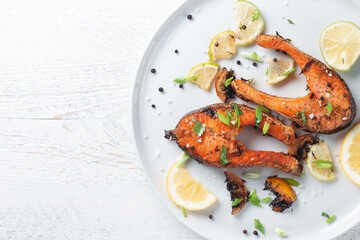 Grilled salmon steak with lemon, spices and lime in a white plate on a light wooden table. Deliciously cooked salmon fillet.