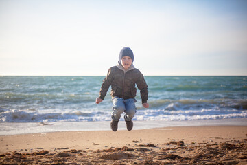 Little boy jumping wirh fun in the sea shore on windy day.