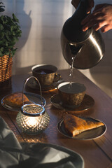 A cozy image of tea time. A woman makes a tea for two. Flat lay of teacups,  sweet pie, and candle.  Cozy tea party concept.