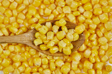 A heap of boiled sweet corn with a wooden spoon on a white table