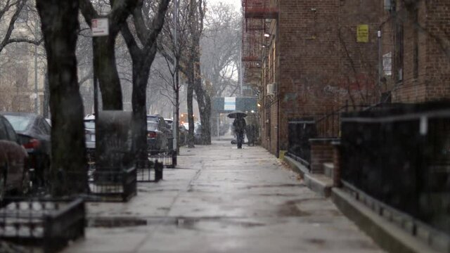 Pedestrian with umbrella walking down Brooklyn street, during a snowy cold New York day - Long Medium shot