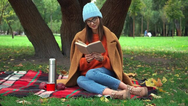 woman in autumn outfit reading book during picnic in park