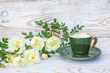 Vintage cup of coffee and wild white rose flowers on rustic white wooden background
