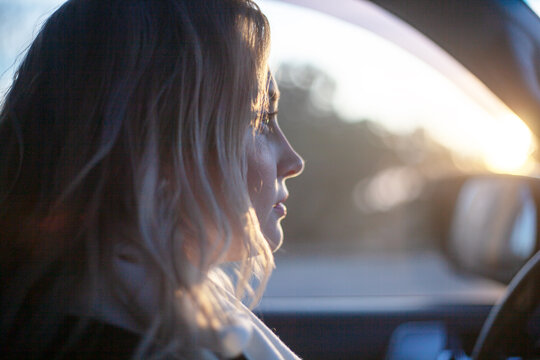 Blond woman dressed black jacket driving a car against the sun lights
