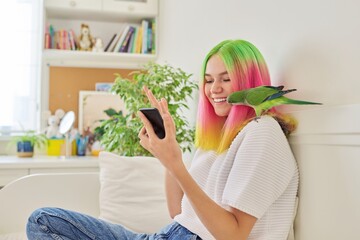 Trendy teen girl with smartphone and quaker parrot on her shoulder