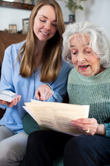 Woman Helping Senior Neighbor With Bills And Paperwork
