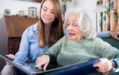 Grandmother Looking At Photo Album With Adult Granddaughter At Home