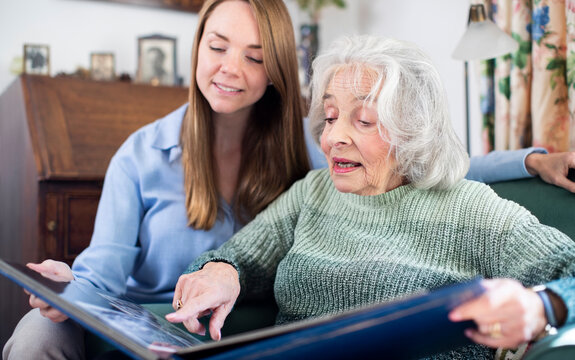 Grandmother Looking At Photo Album With Adult Granddaughter At Home