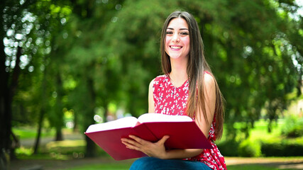 Obraz premium Beautiful female college student reading a book on a bench in a park