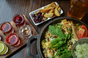 Appetizing pan with fried potatoes with meat and cheese, supplemented with greens, salad and tomato and snacks with alcohol drinks