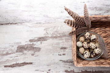 Quail eggs in a glass bowl and feathers in water hyacinth rectangular storage basket on wooden table