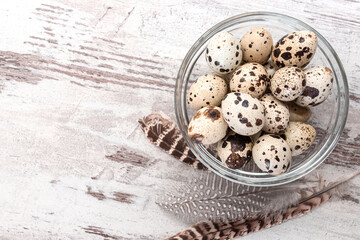 Quail eggs in a glass bowl and feathers on wooden table