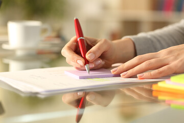 Woman hand writing on sticky note on a table at home