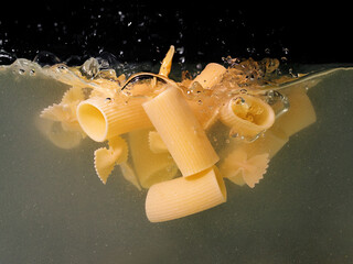 pasta rings and butterflies falling in the boiling water on dark background. Underwater view. Cooking, cooking at home