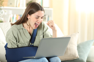 Excited disabled woman with broken arm reading news on laptop