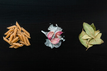 Pasta, garlic and laurel leafs on a black background