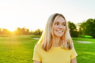 Outdoor portrait of smiling teenage girl 16, 17 years old in yellow T-shirt, on green sunny lawn
