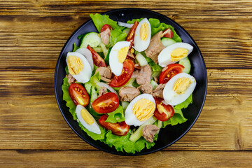 Tasty tuna salad with eggs, lettuce and fresh vegetables on wooden table. Top view