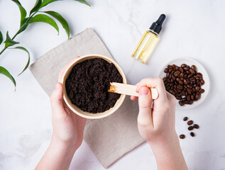 Home skin care. A young woman mix a homemade coffee scab with olive oil on marble background