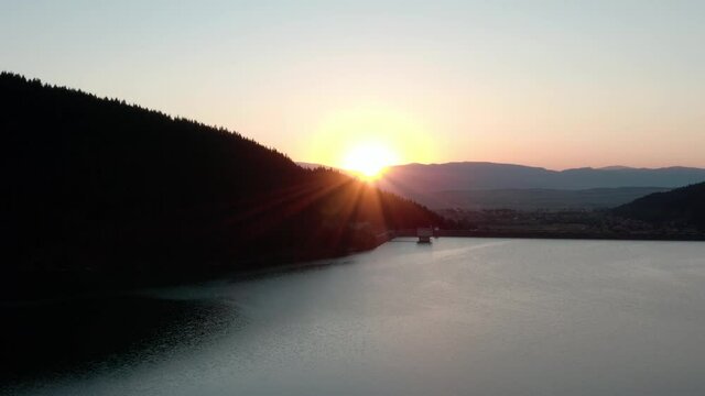Aerial crane shot of sun setting behind ridge over picturesque mountain lake