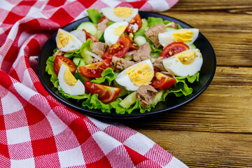 Tasty tuna salad with eggs, lettuce and fresh vegetables on wooden table