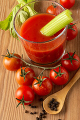 Aerial view of glass with tomato and celery juice, on wooden table with cherry tomatoes, pepper and wooden spoon, selective focus, vertical