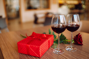 Romantic dinner. Two glasses of wine, red rose red gift box on wooden table.  Valentine's Day, holiday and surprise concept.