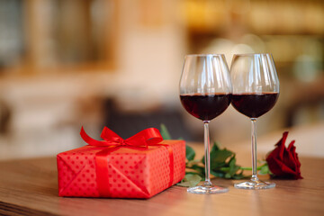 Romantic dinner. Two glasses of wine, red rose red gift box on wooden table.  Valentine's Day, holiday and surprise concept.