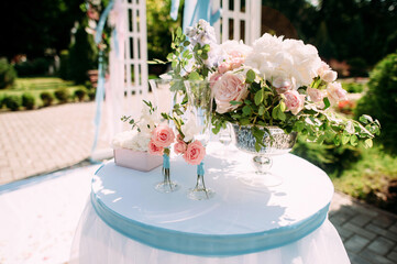 Wedding ceremony details in pink and blue colors. White wedding arch, natural flowers decorations, champagne glasses on green background. Bright summer wedding day