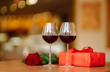 Romantic dinner. Two glasses of wine, red rose red gift box on wooden table.  Valentine's Day, holiday and surprise concept.