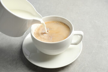 Pouring milk into cup of hot coffee on grey table