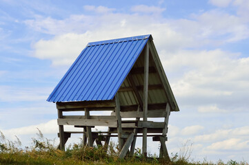 close-up - an old wooden gazebo with a blue gable roof in a recreation field