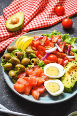 Ketogenic, paleo diet lunch bowl with salted salmon fish, lemon, avocado, olives, boiled egg, tomato, green lettuce salad, healthy food