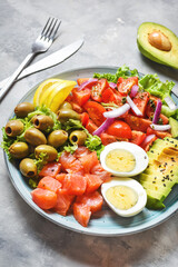 Ketogenic, paleo diet lunch bowl with salted salmon fish, lemon, avocado, olives, boiled egg, tomato, green lettuce salad, healthy food