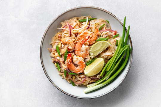 Pad Thai with shrimp, sprouts and green onions on a concrete background, top view