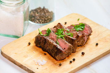 Grilled beef filet Mignon steak or tenderloin on wooden board with pepper, salt and coriander leaves