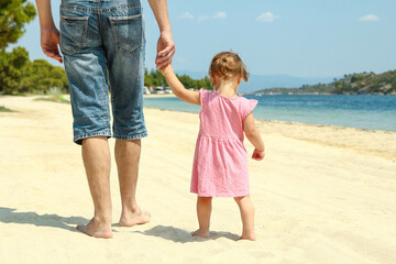 parent father holds the hand of a small child walks on the beach