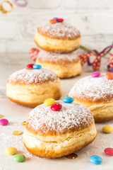 Carnival powdered sugar raised donuts with paper streamers, confetti and chocolate beans on white background, vertical